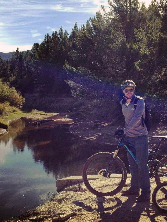 Image of Dr Schicker, an orthopedic surgeon, riding a bike by a body of water and woods